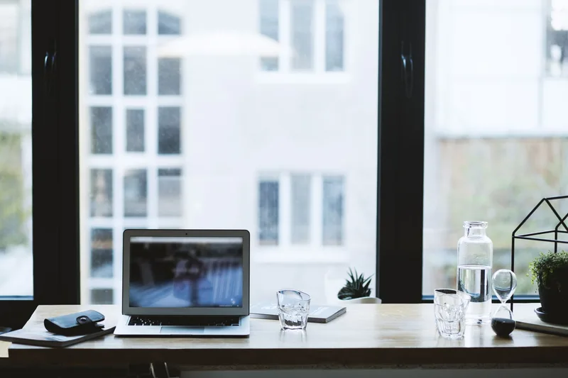 Minimalist bright workspace with a laptop, notebook, and small plant on a clean white desk