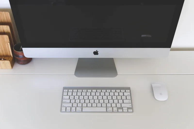 Clean minimal dark home office desk with a large monitor, mechanical keyboard, and desk lamp