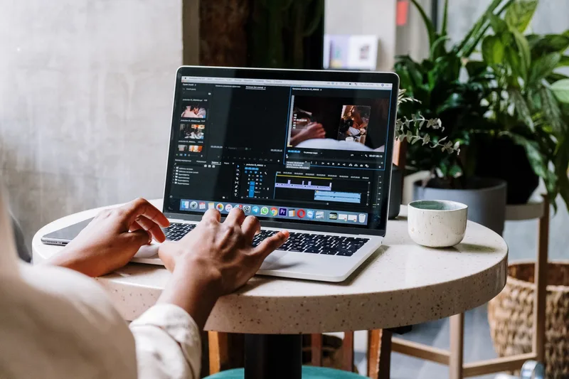 Freelance video editor working on a laptop in a cafe setting using editing software