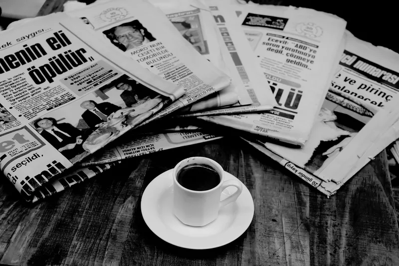 Stack of folded newspapers with a cup of coffee on a wooden table representing print media and news journalism