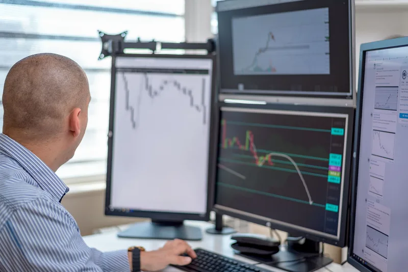 Trader and analyst reviewing financial data on multiple computer monitors in a professional office environment