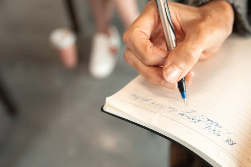 Close-up of a hand writing notes in a notebook with a pen, representing the scripting step for faceless short-form video