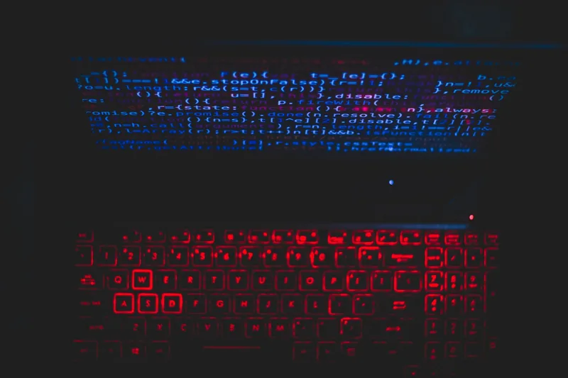 Dark-themed laptop with glowing keyboard and code on screen representing tech content production
