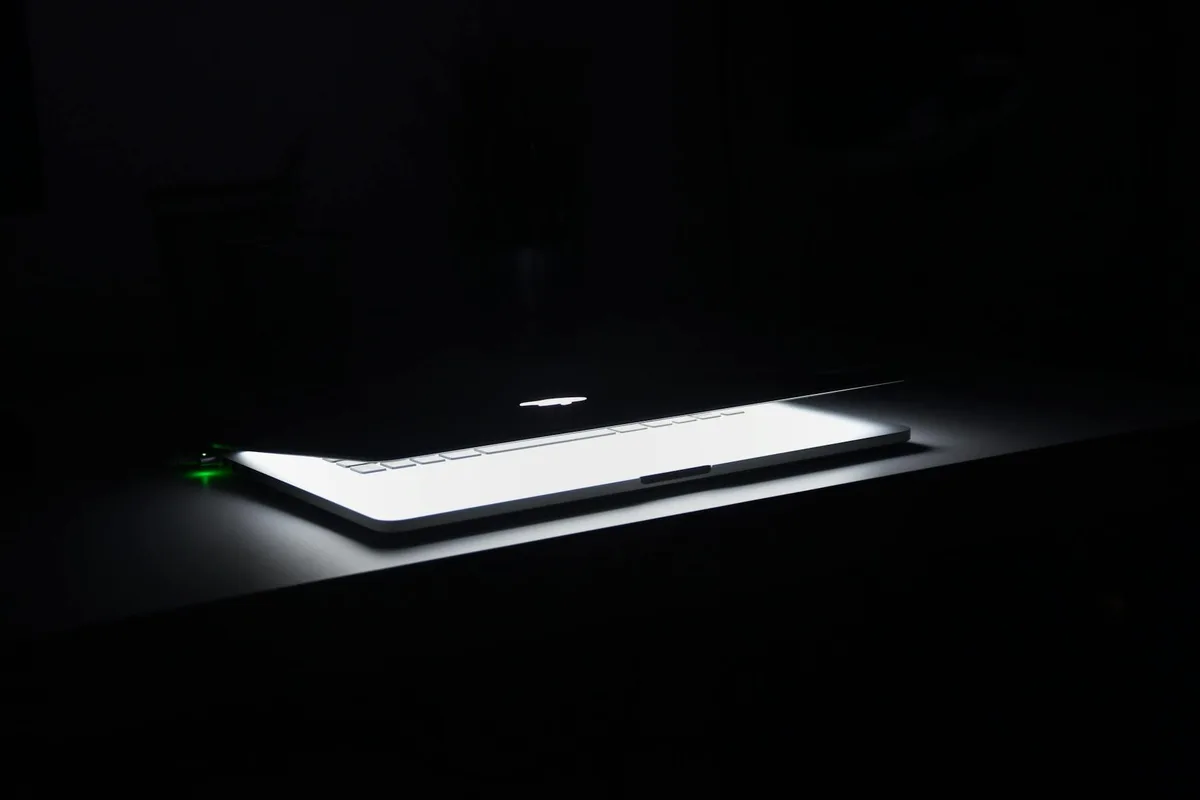 Laptop with glowing keyboard open on dark desk representing faceless content creation workspace